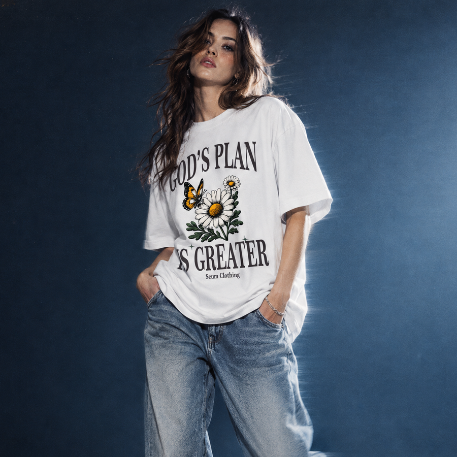 A woman modeling an oversized white graphic T-shirt with distressed blue jeans and white sneakers, standing in a dark studio setting with dramatic spotlighting.