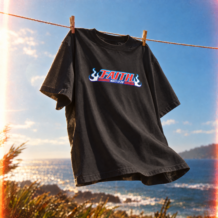 A black t-shirt hanging from a clothesline with wooden clips, featuring a 'FAITH' graphic in red, white, and blue, set against a coastal background with the ocean and sky, inspired by the anime Bleach.