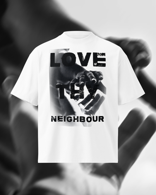 A white short-sleeve T-shirt with a large black graphic print on the front featuring the words 'LOVE THY NEIGHBOUR' over a hand image, shown against a blurred grayscale background of hands.