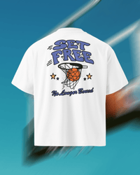 White short-sleeve t-shirt shown from the back, featuring a colorful graphic print with the words 'SET FREE' in blue-purple bubble letters, a basketball going through a hoop, two yellow stars, and 'No Looner Bound' in dark script below. The shirt is centered against a stylized blue background with blurred basketball elements.